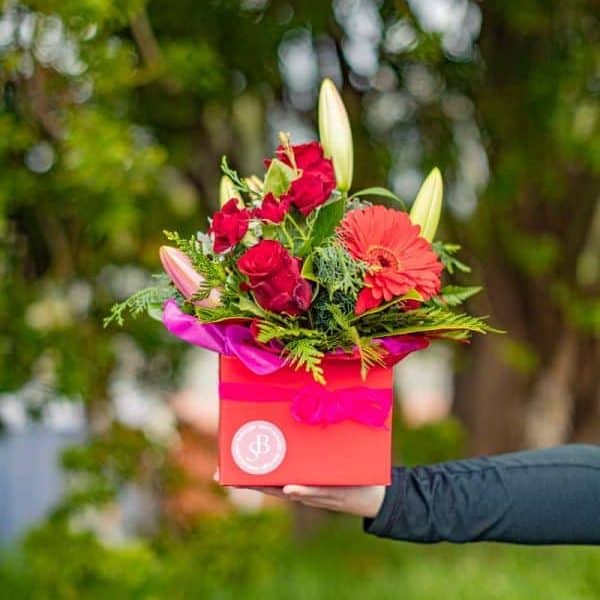 Vibrant floral arrangement in a pink box, featuring roses, lilies, and gerbera daisies, perfect for gifting.
