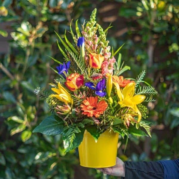 Vibrant mixed flower bouquet in yellow pot with lilies and gerbera, garden or floral arrangement, outdoor garden setting.