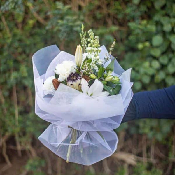Elegant white floral bouquet with lilies and greenery in gift wrap.