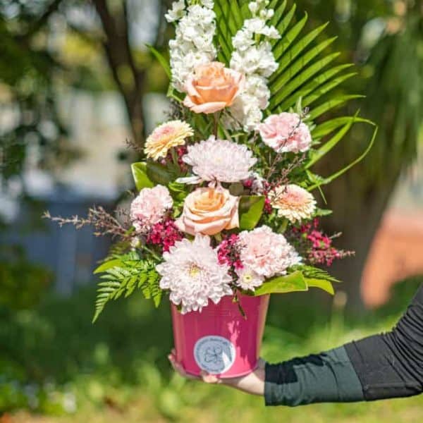 Vibrant floral arrangement with roses, chrysanthemums, and lush greenery in a pink pot.