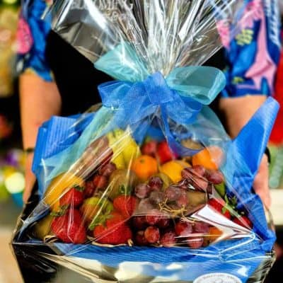 Vibrant fruit gift basket wrapped in clear cellophane with a blue ribbon, featuring fresh strawberries, grapes, and citrus fruits.