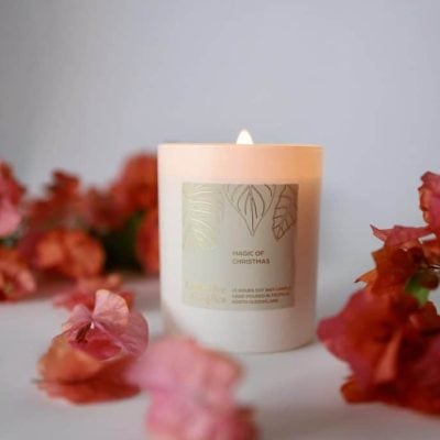 Soft white candle with floral label surrounded by pink flowers and petals on a white surface in a calming setting.