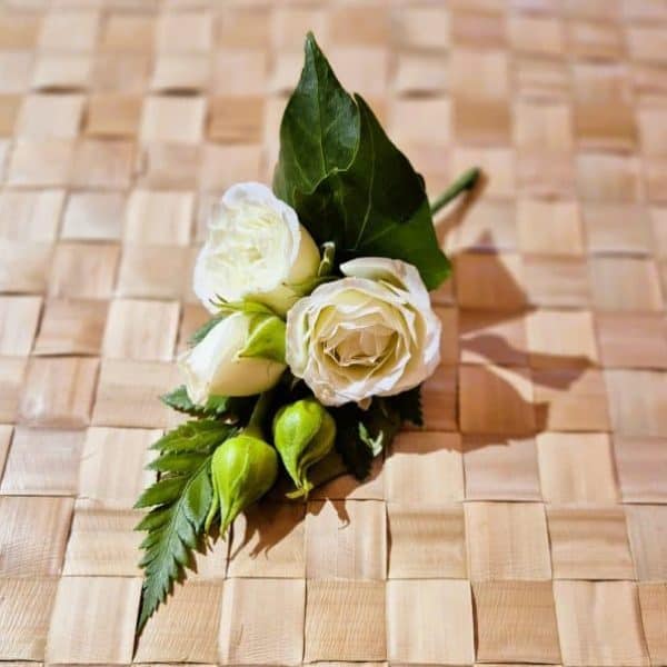 White rose and greenery boutonnier on a woven wooden background.