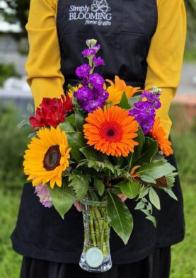 1. posy in a vase Vibrant mixed flower bouquet with sunflowers, gerbera daisies, and purple blooms in a glass vase.