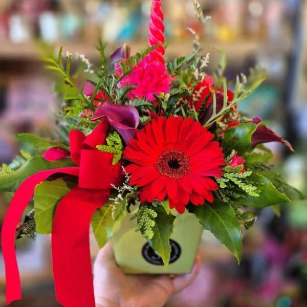 Petite Table Arrangment for Christmas Vibrant red and pink floral arrangement with gerbera daisies, calla lilies, and greenery in a green pot.