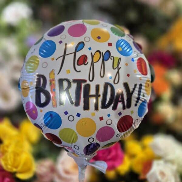 Happy birthday balloon with colourful confetti design in front of blooming flowers.