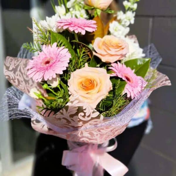 Pink and peach flower bouquet with roses and gerbera daisies, wrapped in decorative paper.