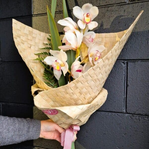 White orchids bouquet with greenery, wrapped in woven paper, perfect for floral gifting and decorations.