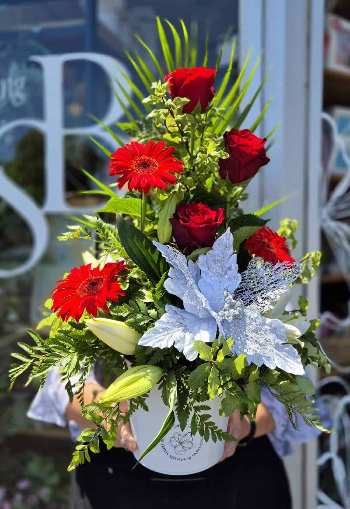 Bright red roses and gerbera daisies in a Christmas-themed floral arrangement with silver foliage.
