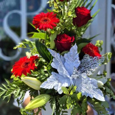 Vibrant red roses and gerbera daisies in a festive Christmas floral arrangement.