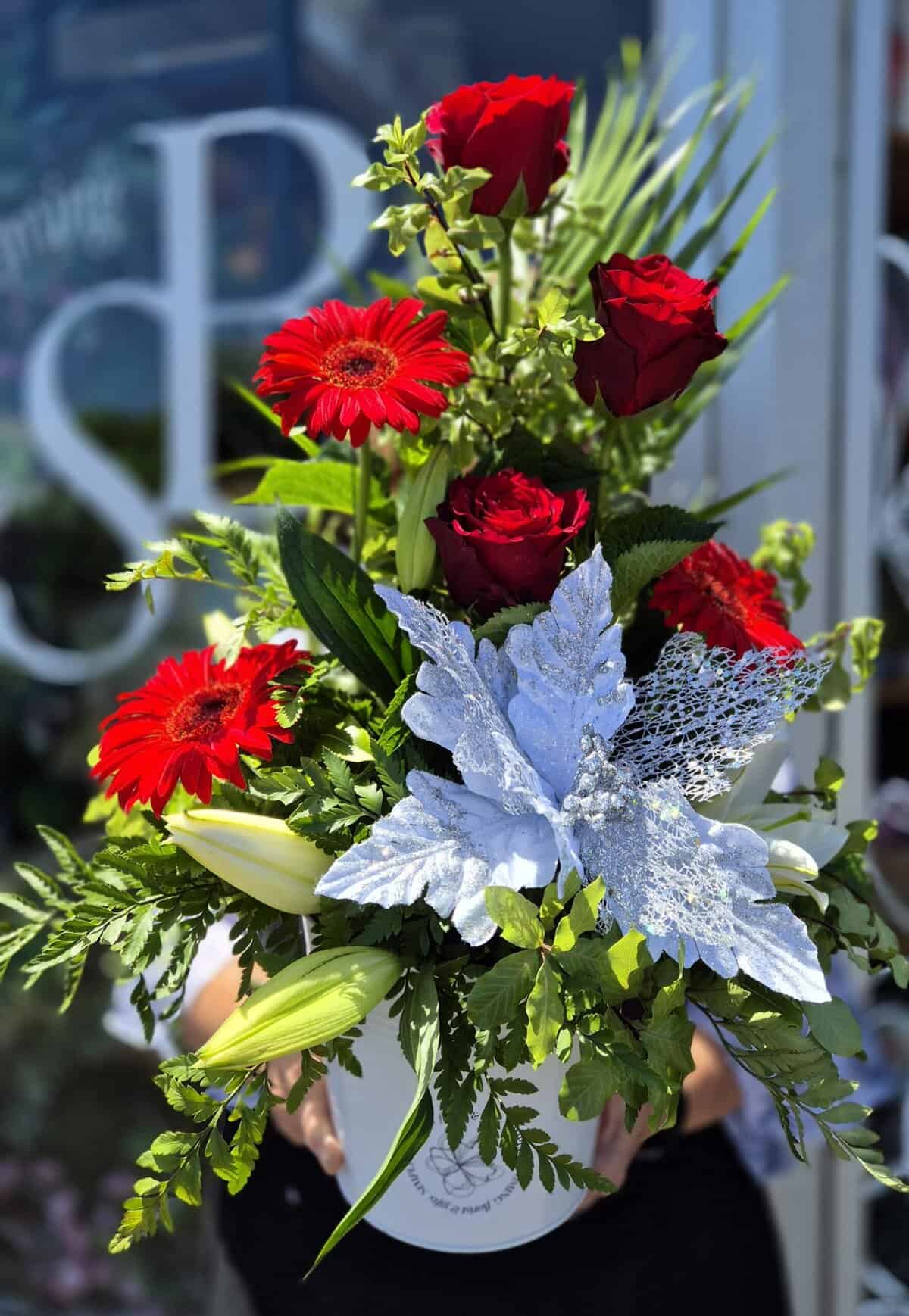 Vibrant red roses and gerbera daisies in a festive Christmas floral arrangement.