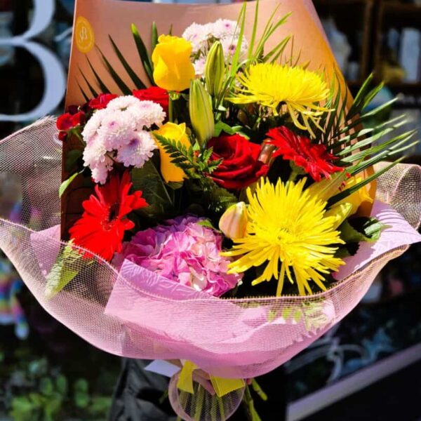 Colourful bouquet of fresh roses, chrysanthemums, lilies, and greenery in pink wrapping.