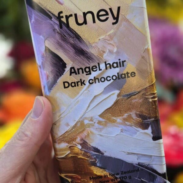 A person holding a Fruney Angel Hair Dark Chocolate bar with colorful flowers in the background, showcasing the product's artistic packaging.