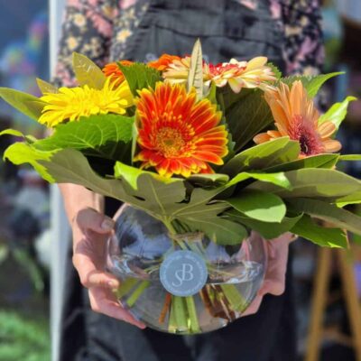 Bright gerbera daisies and sunflowers in a glass vase, vibrant floral display.