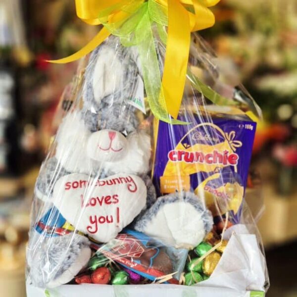 Cute bunny plush toy with chocolates and snacks in a gift basket.