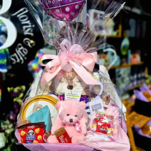 Adorable baby girl gift basket with teddy bear, toys, and pink decorations for new arrivals.