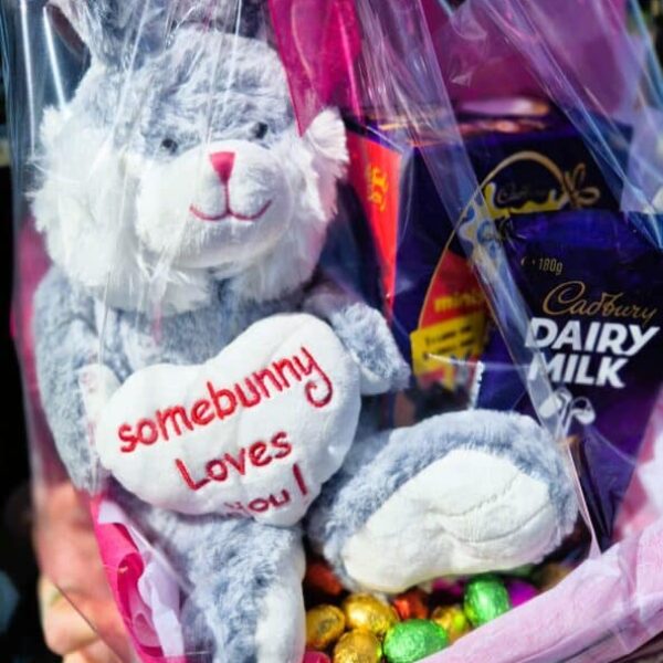 This image features a soft plush bunny holding a heart that says "somebunny loves you," surrounded by chocolates and Cadbury Dairy Milk bars, ideal fo.