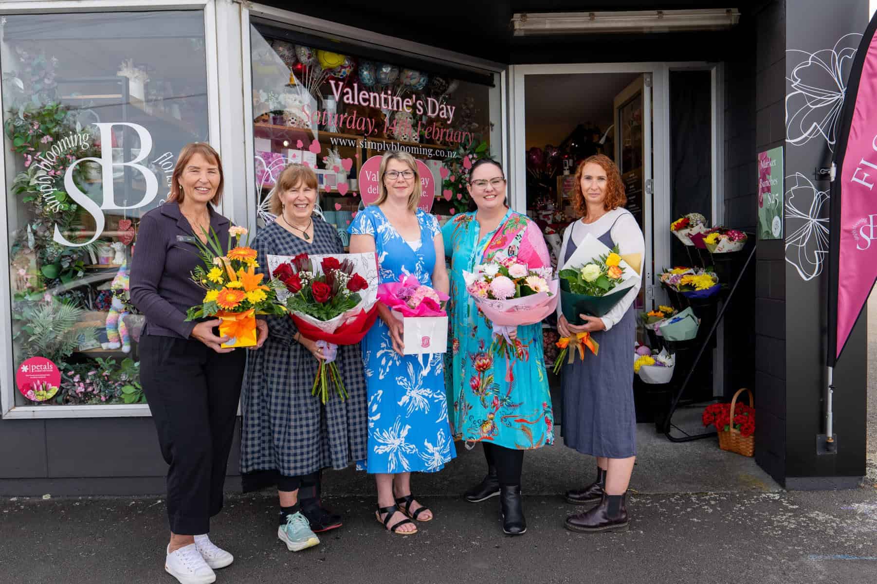 Women celebrating with flowers in front of Simply Blooming shop.