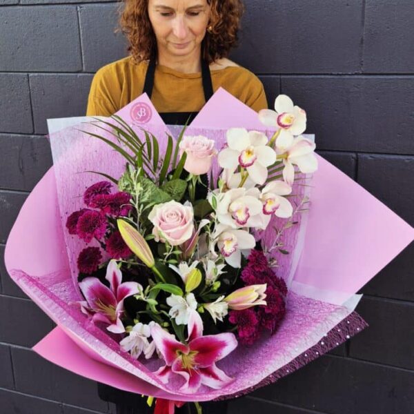 Elegant floral arrangement featuring orchids, lilies, and roses in pink wrapping.