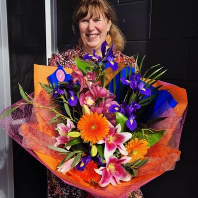 Bright floral bouquet featuring pink lilies, purple irises, orange gerberas, and greenery.