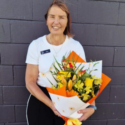 An experienced florist holding a vibrant bouquet of yellow and orange flowers, smiling against a dar.
