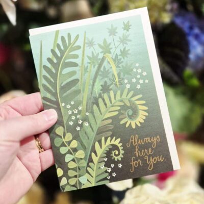 Hand holding a Simply Blooming greeting card with lush green foliage design.