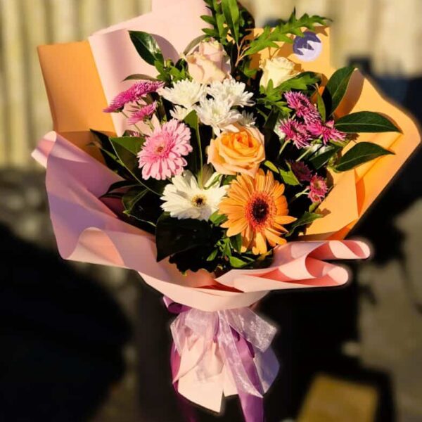 Beautiful spring floral bouquet featuring roses, daisies, and lush greenery wrapped in pink paper.