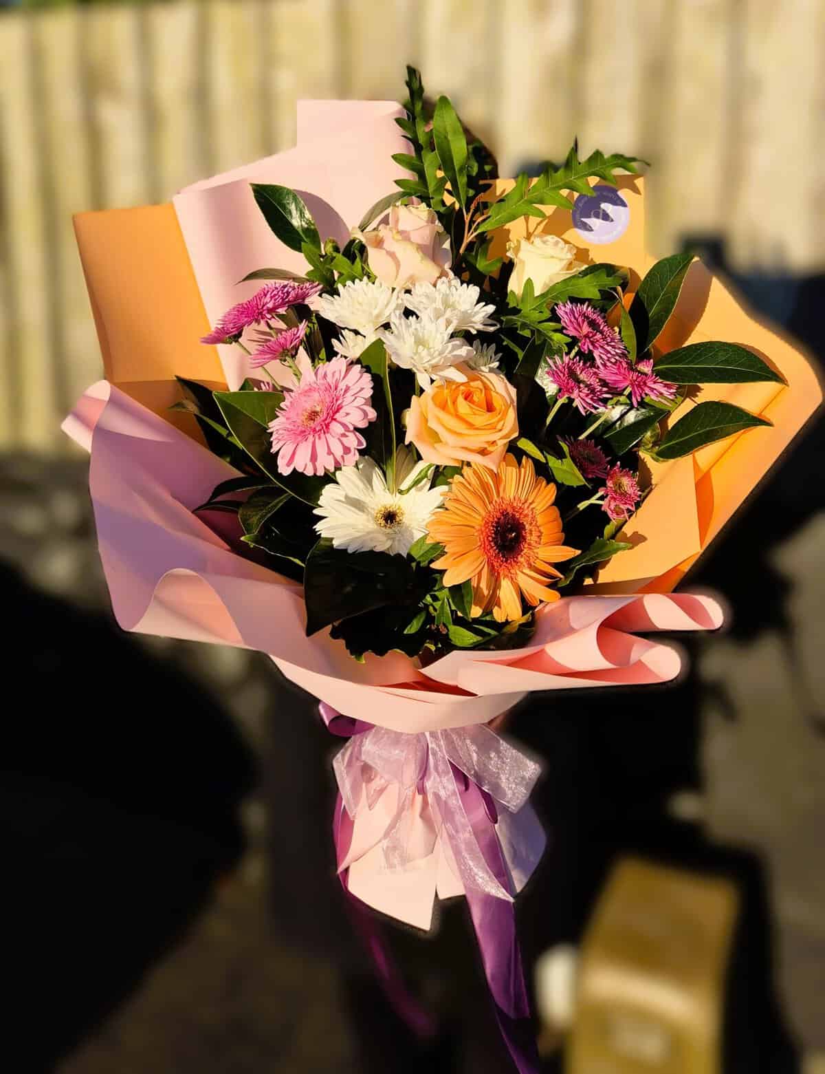 Beautiful spring floral bouquet featuring roses, daisies, and lush greenery wrapped in pink paper.