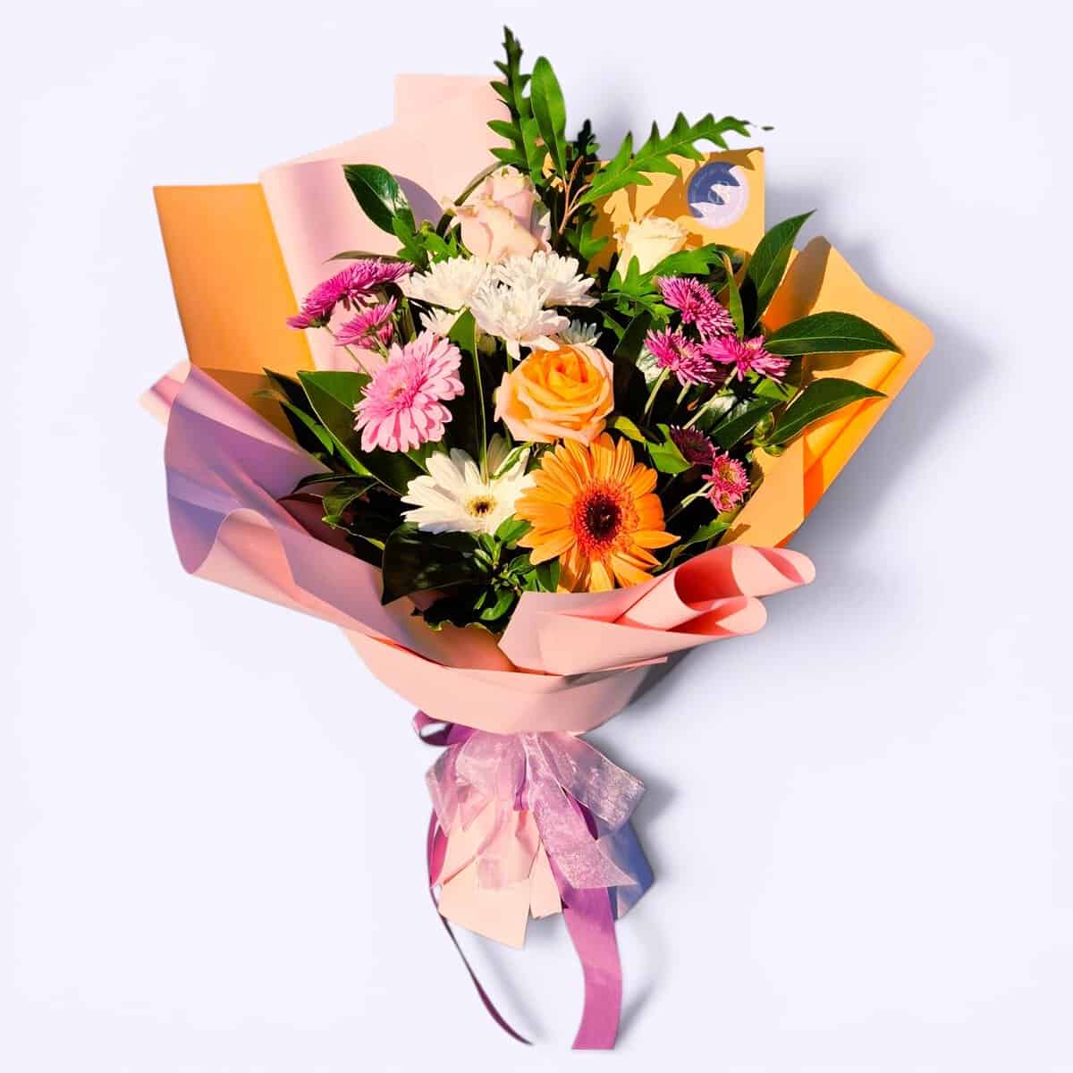 A vibrant mixed flower bouquet featuring roses, daisies, and greenery, wrapped in pastel paper with.