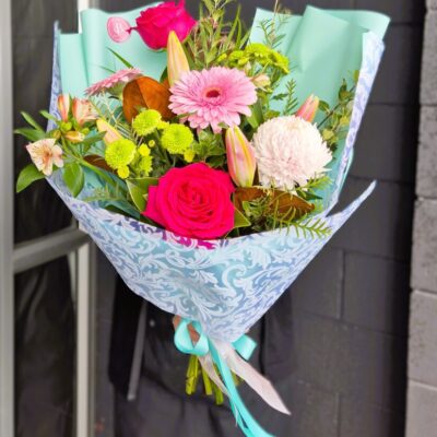 Vibrant mixed flower bouquet with roses, gerbera, lilies, and greenery, wrapped in decorative paper,.