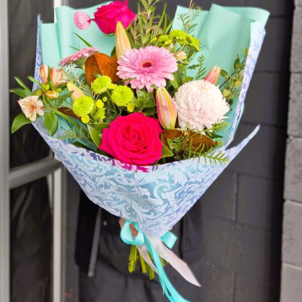 Vibrant mixed flower bouquet with roses, gerbera, lilies, and greenery, wrapped in decorative paper,.