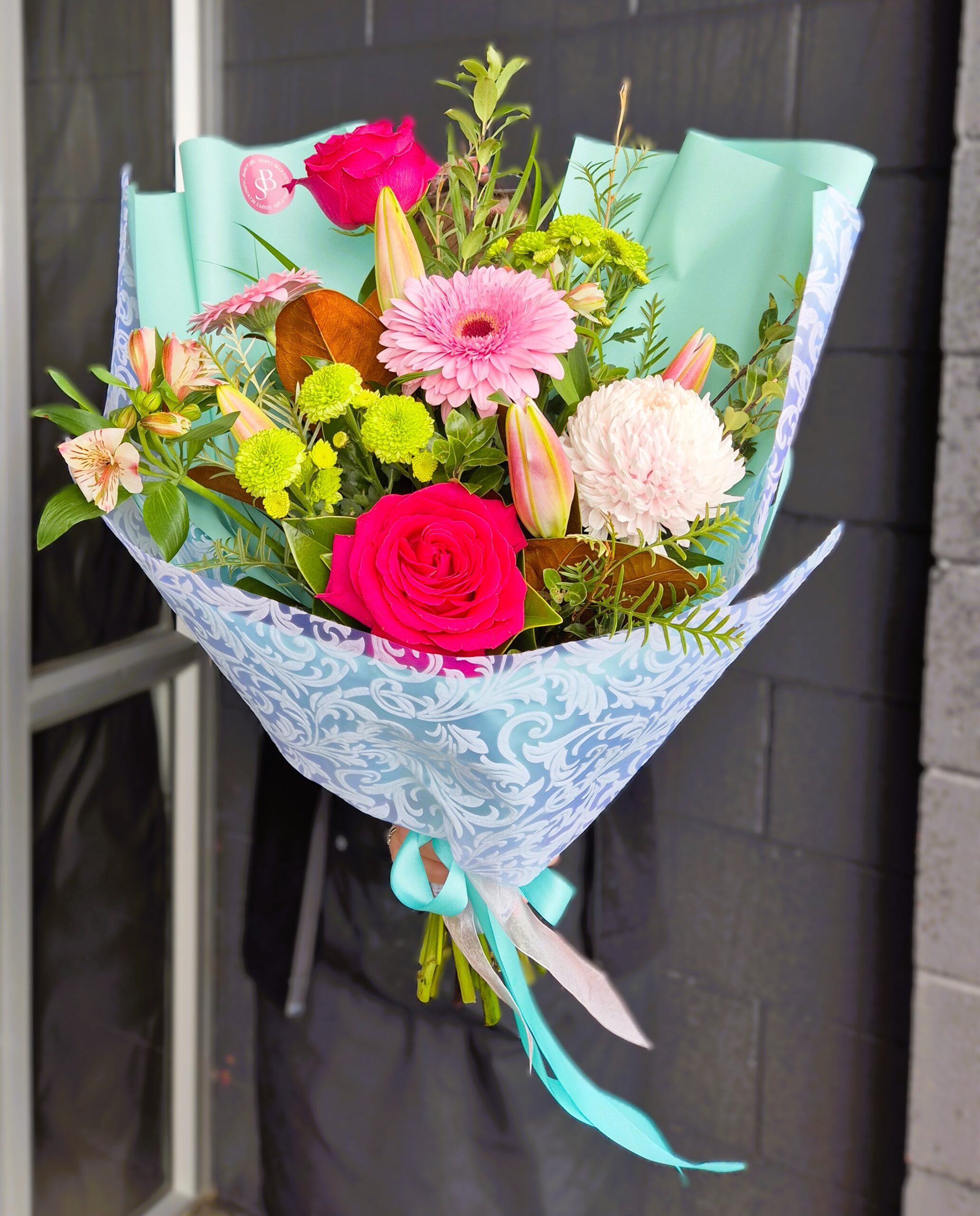 Vibrant mixed flower bouquet with roses, gerbera, lilies, and greenery, wrapped in decorative paper,.